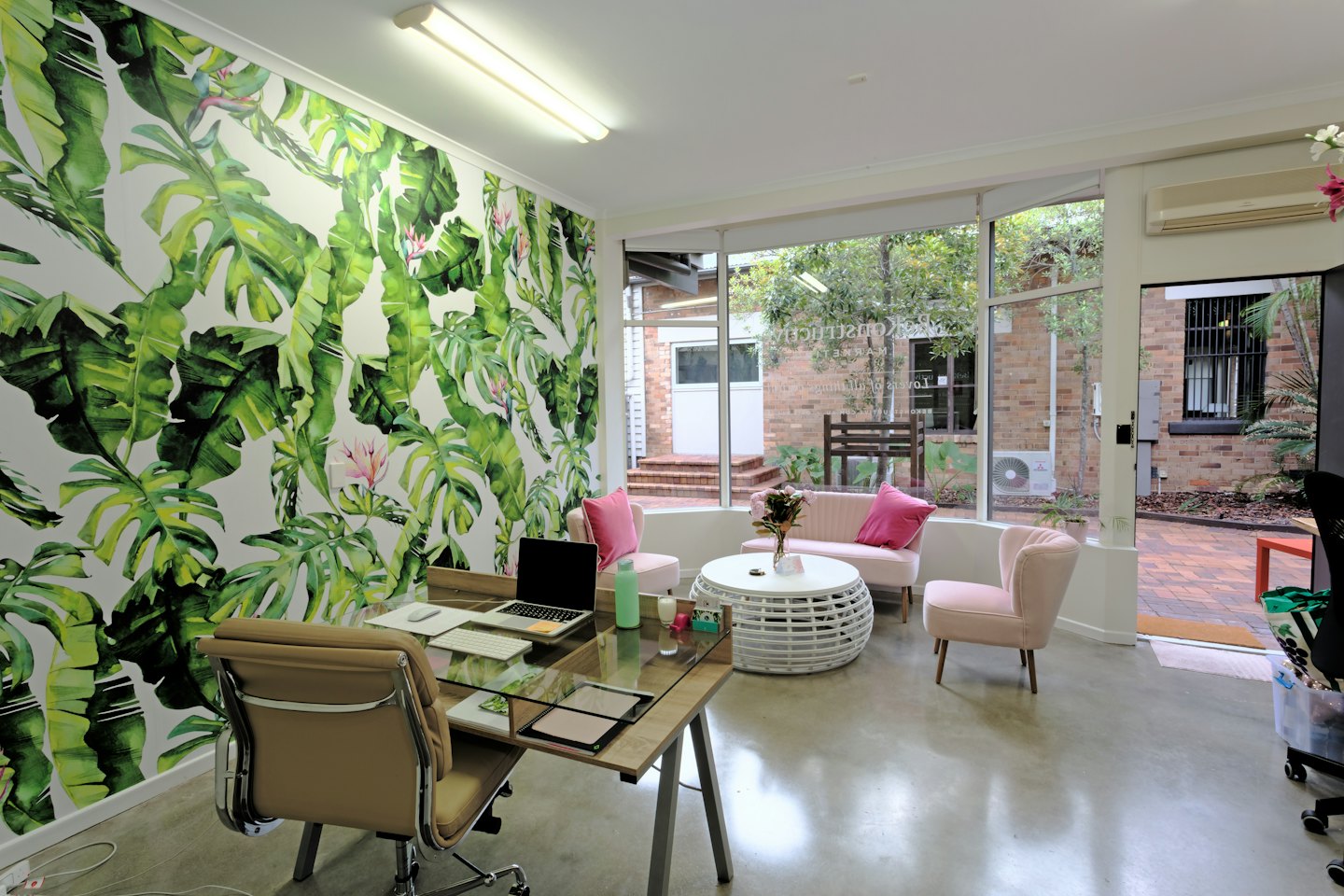 Modernes Bürointerieur mit rosa Stühlen und tropisch gemusterter Tapete.