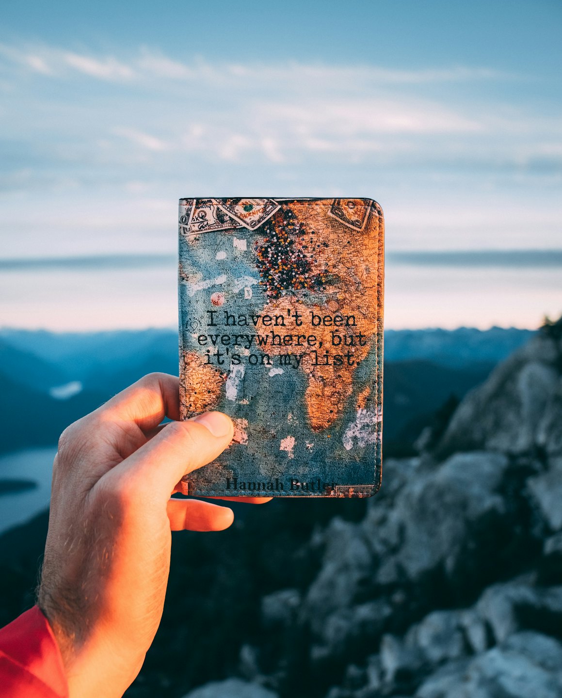Hand hält einen Reisepass mit Weltkarte und Reise-Zitat.